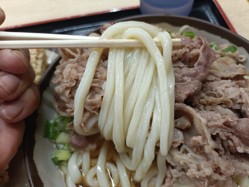 高松うどん巡り手打ちうどん上田の丼から溢れるほどの肉がのった季節限定肉ぶっかけうどんの麺を箸ですくいあげる